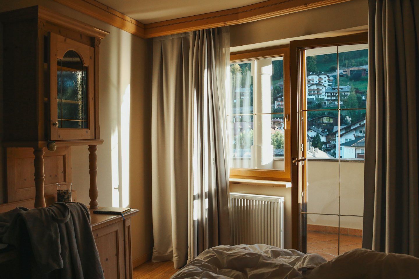 Camera da letto illuminata dal sole con vista sul villaggio attraverso la porta aperta del balcone.